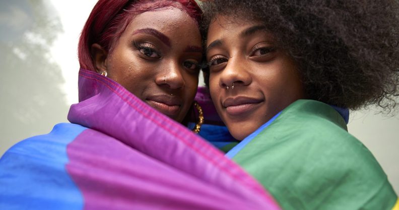 Two women draped in a rainbow Pride flag.