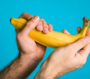 A person holds a yellow banana in both hands in front of a light blue background