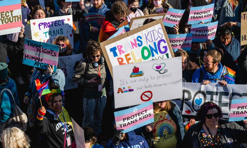 A crowd of people, many of whom are young, hold up signs in support of the LGBTQ+ community and trans youth as they protest the passing of SB 150 at the Kentucky state capitol