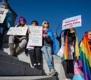 A crowd of people hold up LGBTQ+ and trans Pride flags as well as signs in support of the community as they sit on the Kentucky state capitol steps to protest against the passing of SB 150