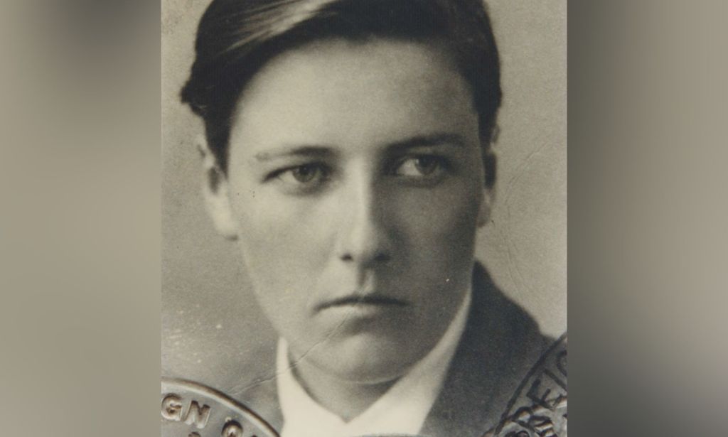 A black and white photo of trans trailblazer Michael Dillon wearing a white shirt and dark blazer from around the time he left Oxford