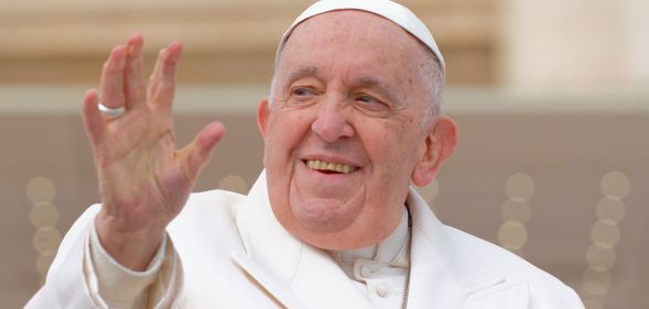 Pope Francis wears a white jacket, white robes and cap as he waves to people gathered in a public audience at the Vatican in Rome