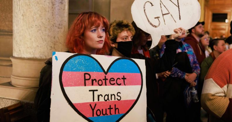 Protesters hold a placard that says, "Protect trans youth" and "Gay" as they protest against Republicans attacking LGBTQ+ rights including education on queer topics and trans healthcare