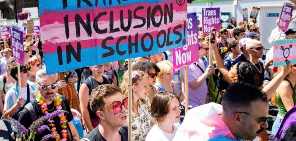 A crowd of people marching with a large trans flag with the words trans inclusion in schools