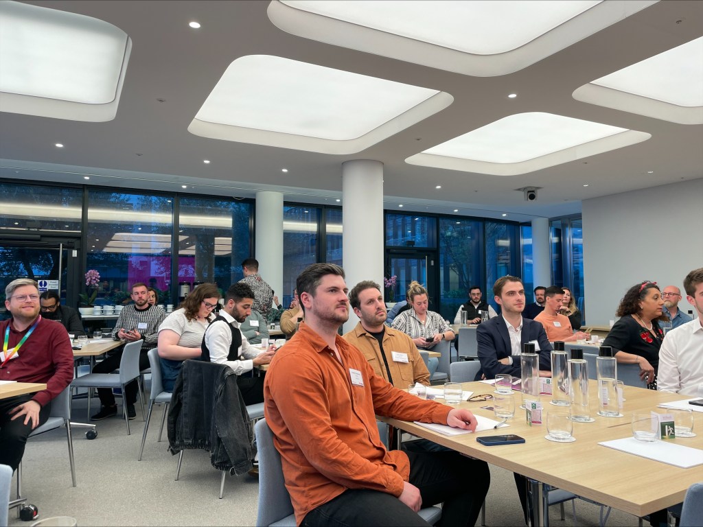 A crowded room of event attendees look on during a presentation.