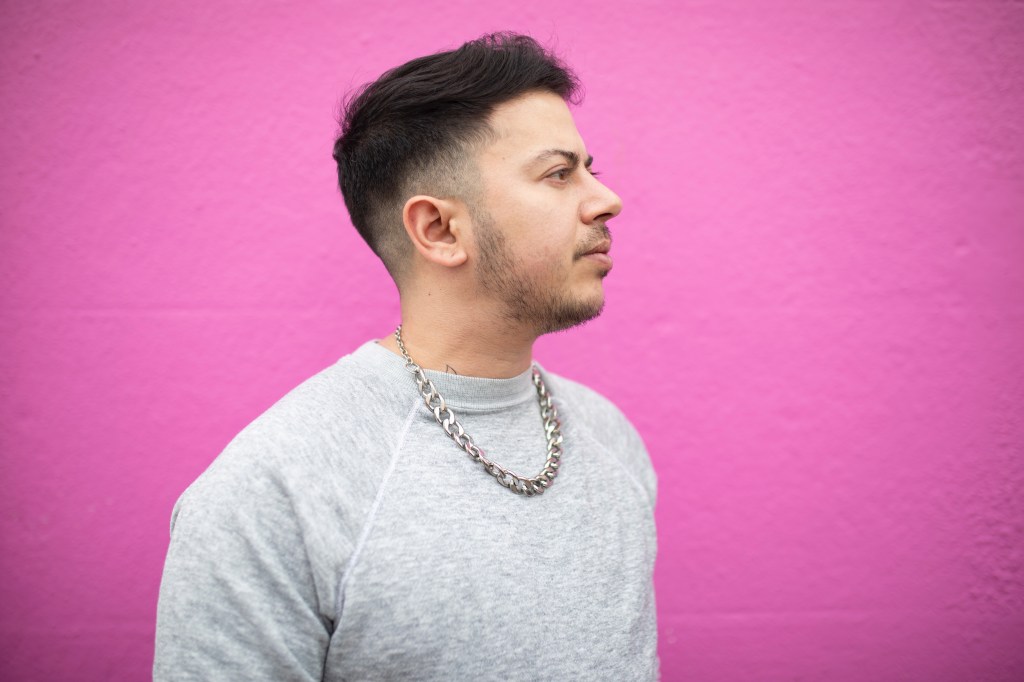 Fox Fisher standing against a pink background.