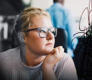 A female presenting person is looking out the window. They have eyeglasses on. They look stressed and there is a creative overlay for visual impact.