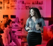 This is a stylised image of a woman speaking to her colleagues at work. Her image is emphasized over a red an orange background