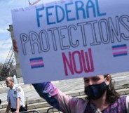 Protester holds up sign reading "federal protections now" with the trans flag
