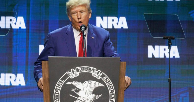 Former president Donald Trump wears a suit and tie as he stands at a podium and speaks into a microphone at the NRA annual conference