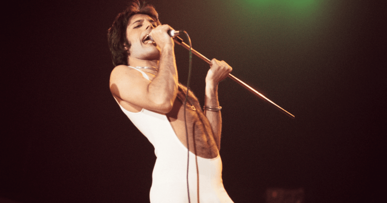 Freddie Mercury wears a white outfit as he sings on stage during a performance with the band Queen