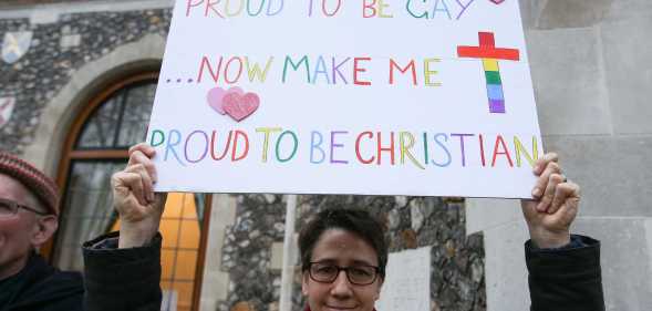 A gay christian holds a sign that reads "proud to be gay, now make me proud to be christian"