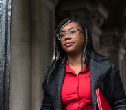 Kemi Badenoch wearing a black blazer and red blouse walking outdoors.