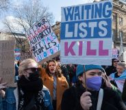 A person holds up a sign in the colours of the trans Pride flag (blue, pink and white) reading 'Waiting lists kill' referring to the huge wait times trans people face accessing gender-affirming healthcare on the NHS