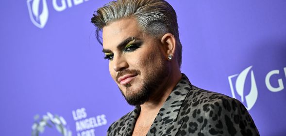 Singer Adam Lambert wears an animal-print shirt and stands against a purple background