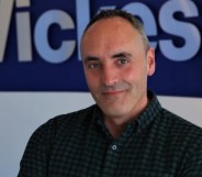 This is a portrait of Ben Jackson. He is wearing a dark shirt and has his arms folded. He is standing in front a Wickes sign.