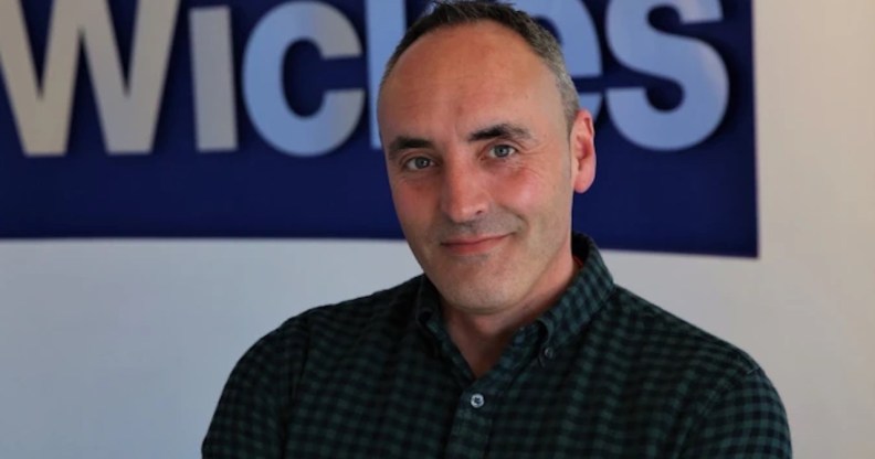 This is a portrait of Ben Jackson. He is wearing a dark shirt and has his arms folded. He is standing in front a Wickes sign.