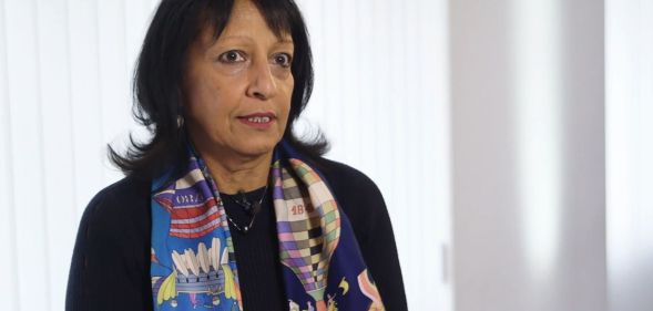 Kishwer Falkner, wearing a multi-coloured scarf, speaks in a white room.