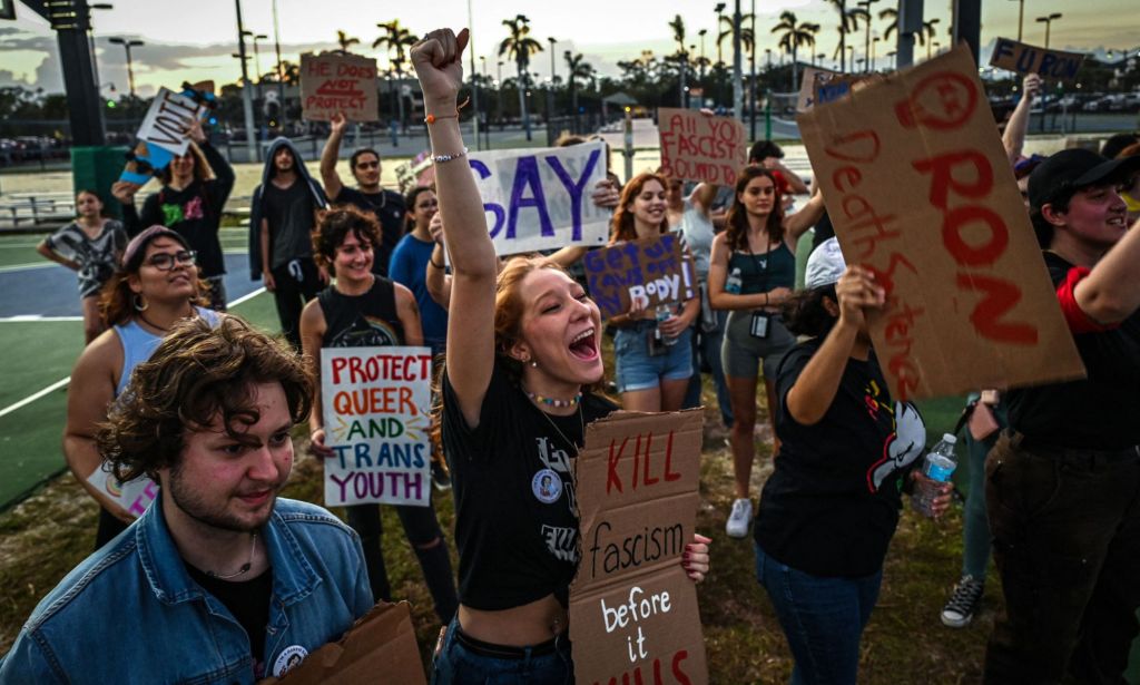 A group of protestors, with one raising their arm, condemn Florida governor ron DeSantis.