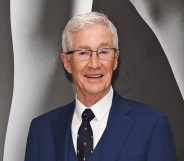 Paul O’Grady wearing a blue suit on a grey background