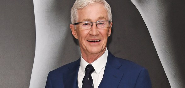 Paul O’Grady wearing a blue suit on a grey background