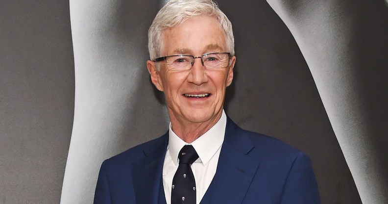 Paul O’Grady wearing a blue suit on a grey background