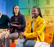 This is an image of a black woman smiling and in the middle of her colleagues. She is wearing bright yellow. The background is creatively accented with the colours of the Pride flag.