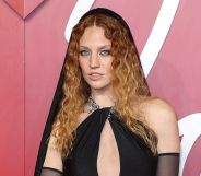 Jess Glynne wears a black dress with chest cutout and black hood.