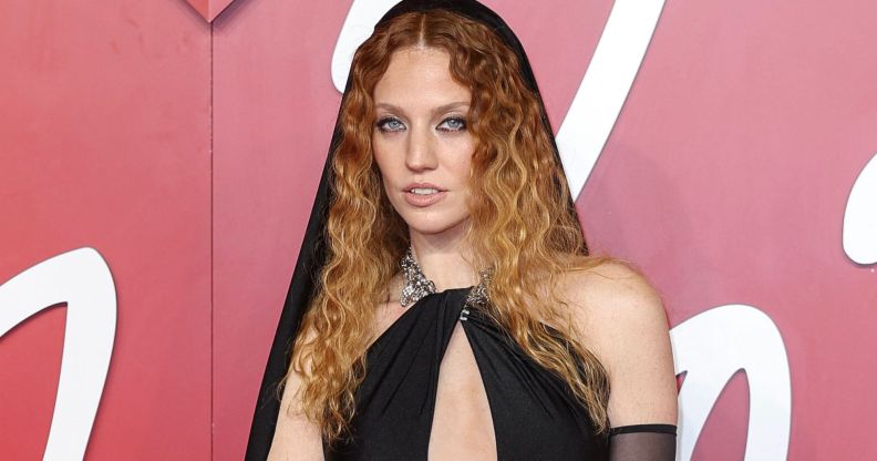 Jess Glynne wears a black dress with chest cutout and black hood.