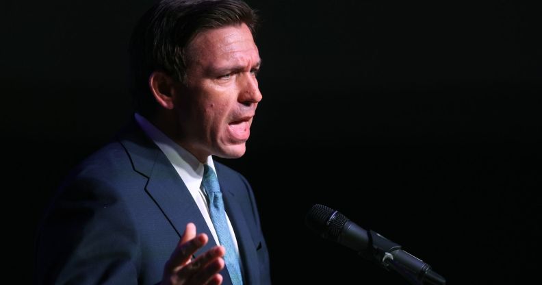 Ron DeSantis, in a blue tie and navy blue suit, speaks infront of a black background.