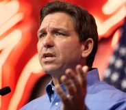 Ron DeSantis speaking to a crowd, with lights and an American flag behind him.