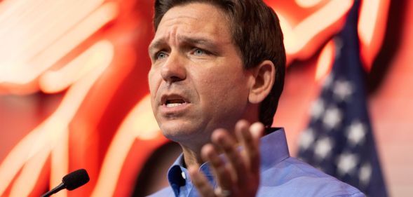 Ron DeSantis speaking to a crowd, with lights and an American flag behind him.