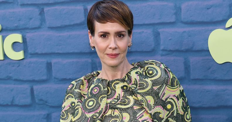 Sarah Paulson wears a patterned green, white and pink top while standing against a blue brick background.