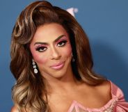 Shangela from the neck up, smiling at the camera, wearing a brown wig and pink make-up.