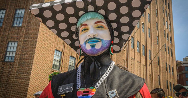 A member of the Sisters of Perpetual Indulgence, wearing an extravagant nun-style costume, glitter beard, and white face paint.