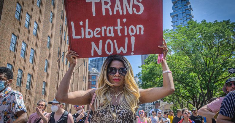 An individual at an LGBTQ+ Pride parade holds a sign of trans solidarity.