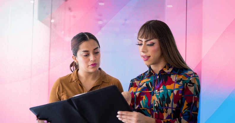 There are two women overlooking a report. One is wearing a brown shirt and the other has a more colourful shirt on. There is a creative background of the trans pride flag colours.