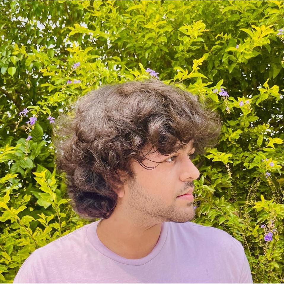 Vaivab Das, an Indian activist, pictured outdoors. They are photographed against a background of green trees with long hair.