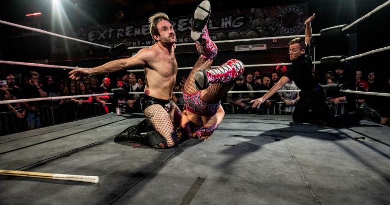 Gay wrestler EFFY kneels in the wrestling ring as he fights his opponent, who has been flipped upside down