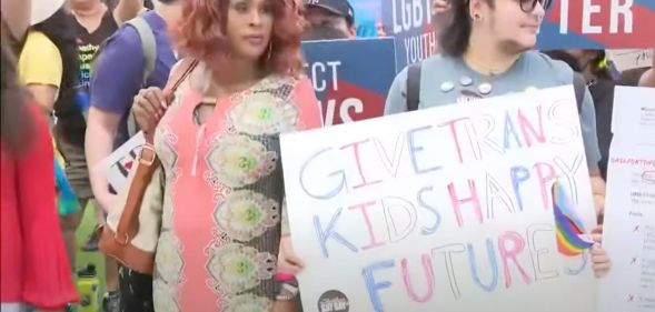 Two people stand amid a protect in Florida holding up a sign reading 'give trans kids happy futures' as the state rolls back access to gender-affirming healthcare for trans youth