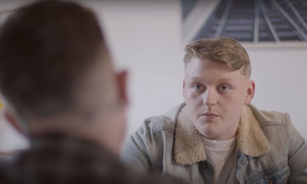 Trans teen Kai wears a white shirt and tan coloured jacket as he is interviewed for a film project by Fox Fisher and My Genderation 