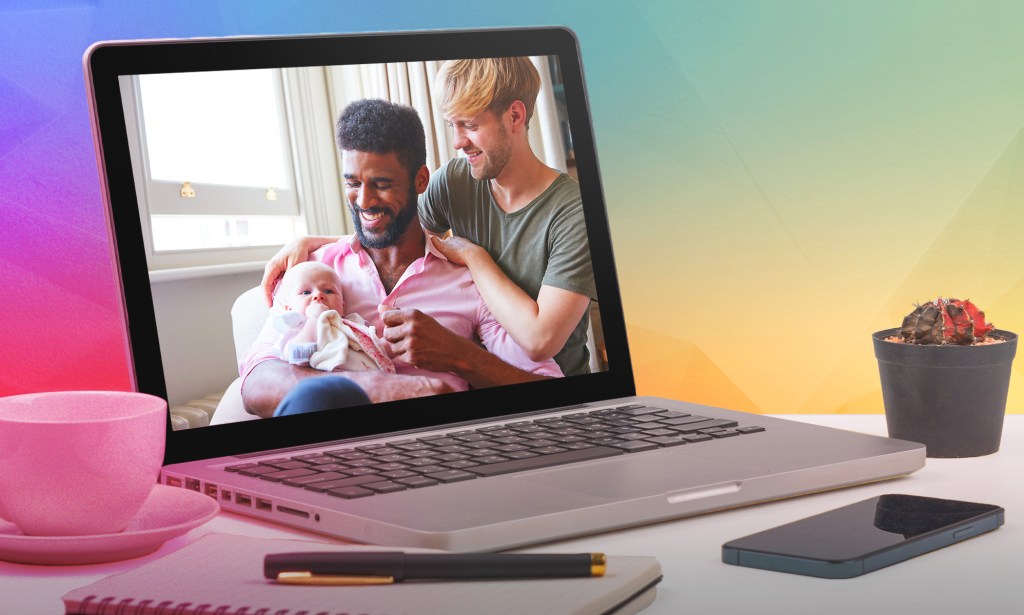 This is an image of a same sex couple with their child. The image is seen on a screen of a macbook pro. The computer is sitting on a desk. 