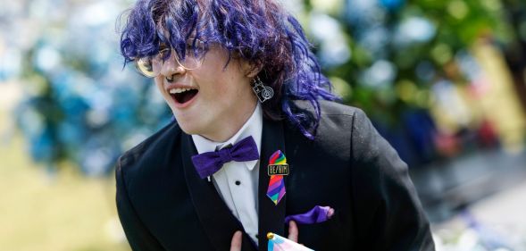 An Arkansas queer young person, wearing a suit and bow tie, leans over with their hands pointing inward.