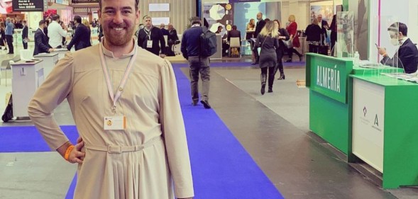 This is an image of Chris King from Lightning Travel Recruitment. They are wearing a white dress and are standing in what looks like a conference hall.