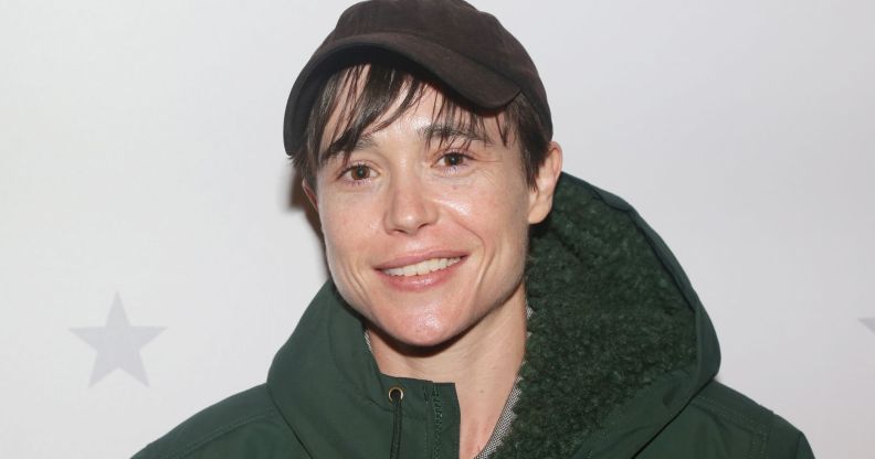 Elliot Page wears a thick green coat and brown cap while smiling at the camera.