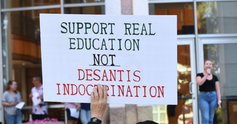 During a Florida protest, a protestor holds up a sign reading "Support real education, not DeSantis indoctrination."