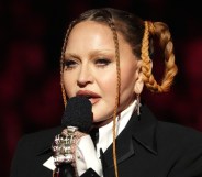 Madonna wears a suit and multiple rings, and she holds a microphone