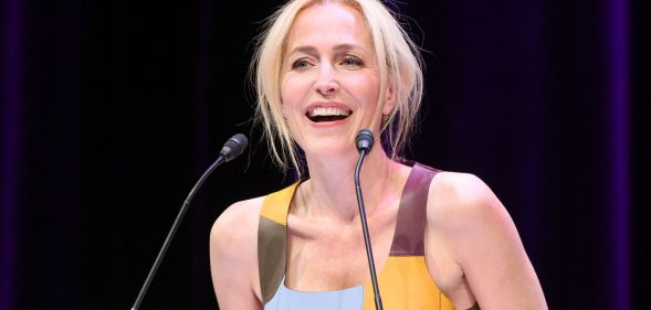 Gillian Anderson in a blue and yellow dress speaking into a microphone.