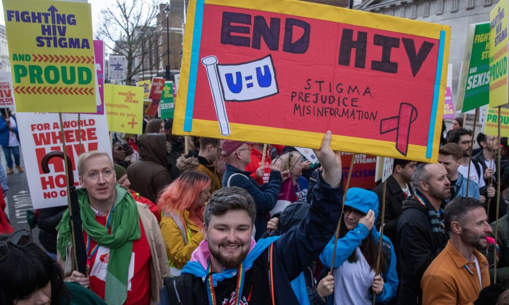 Protestors at a sexual health protest hold signs reading "end HIV, stigma, prejudice, misinformation."