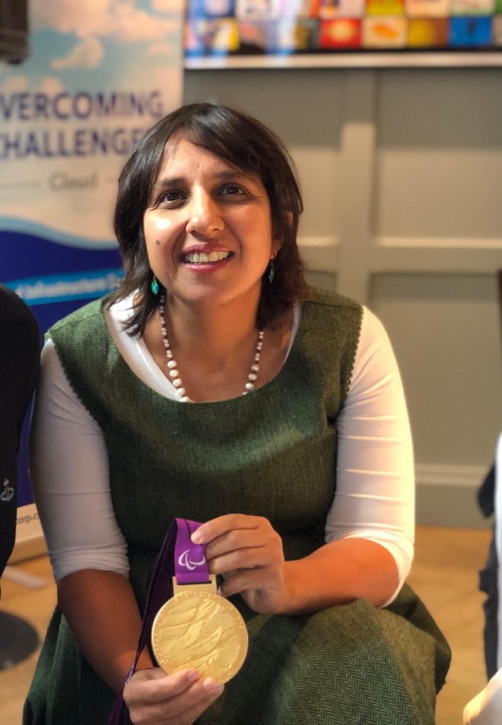 This is an image of Kavita Kapoor, she is wearing a green dress over a white top and is holding a medal. 